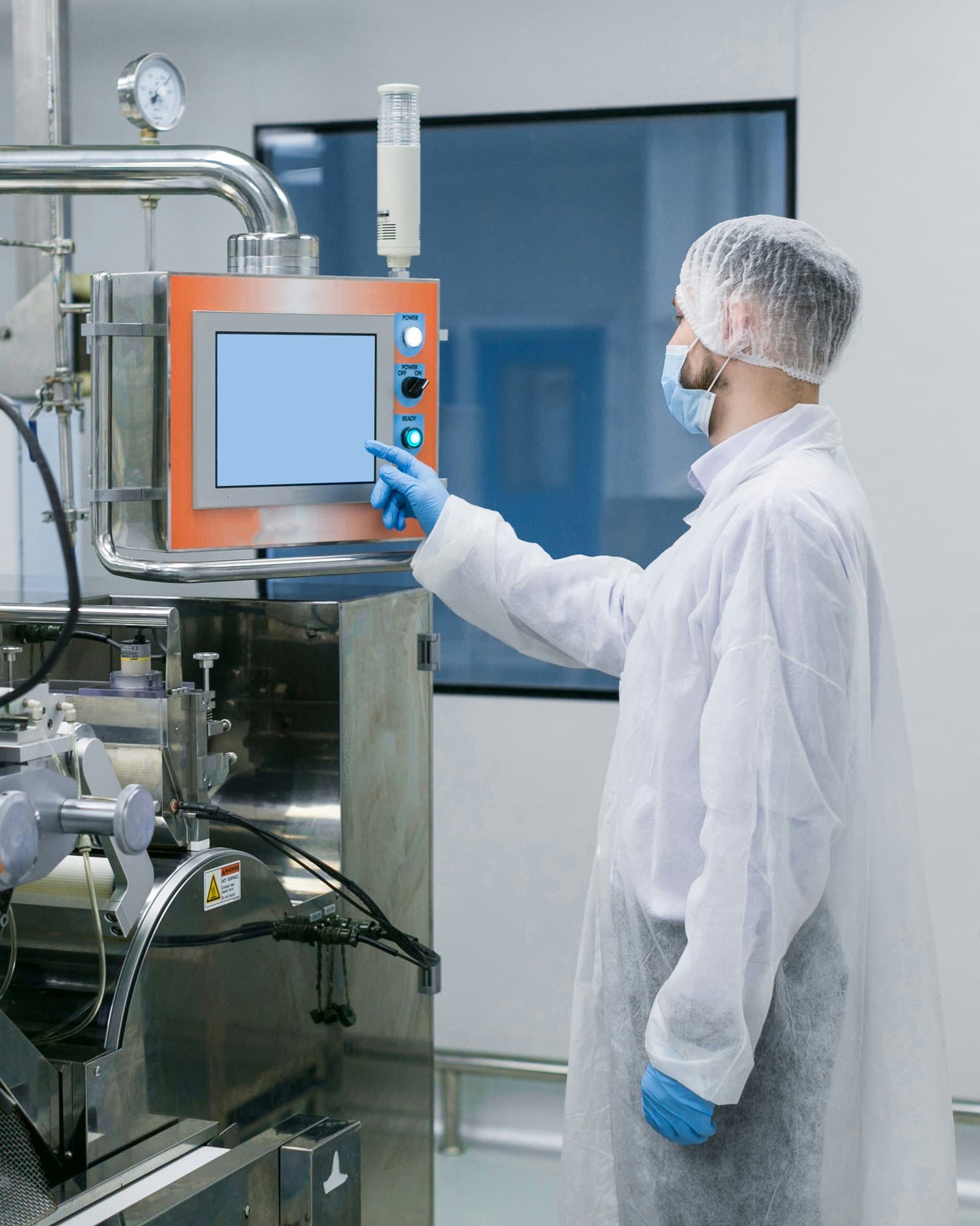 Technician in a cleanroom gown, mask, and gloves working the touchscreen on a stainless process tool