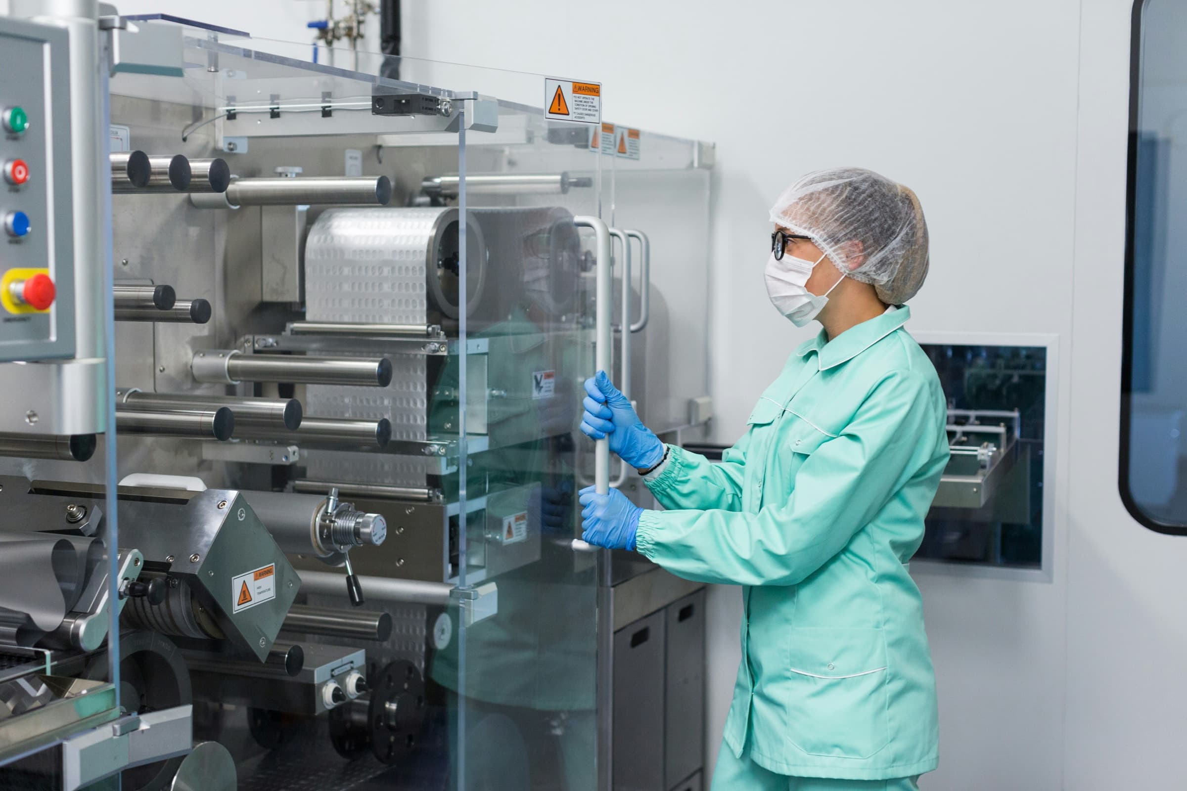 Technician in a cleanroom gown and gloves working at a glass-enclosed process tool